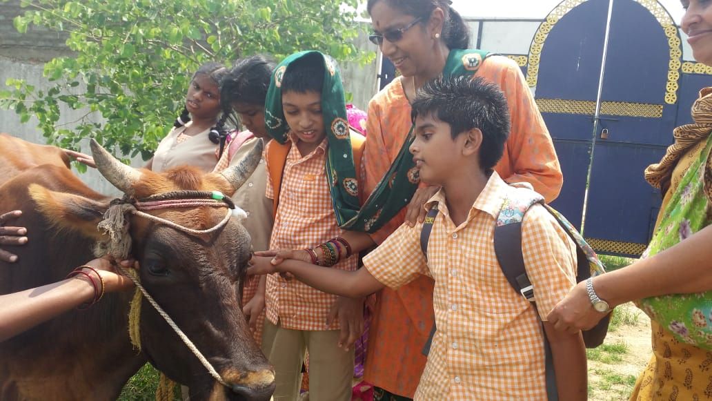 Children and teachers planting saplings together under a tree at Sreyes Farm, smiling and nurturing growth.